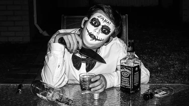 Man wearing a mask with an homage to joker style masks and the word HAHA on their forehead. The man has been drinking a lot and has a knife he is holding.