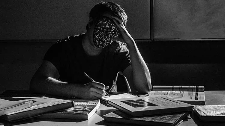 Man with a mask adorned with mathematical equations, writing his thesis.