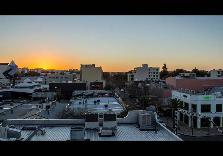 Landscape photo from the roof of a building looking at a sunset over a bunch of other city buildings.