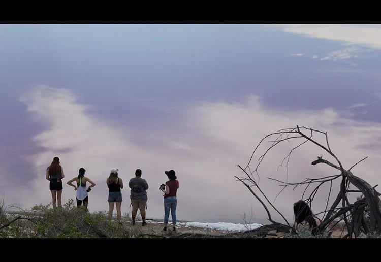 Photo of 6 people looking over at the clear reflection of the sky in a body of water.