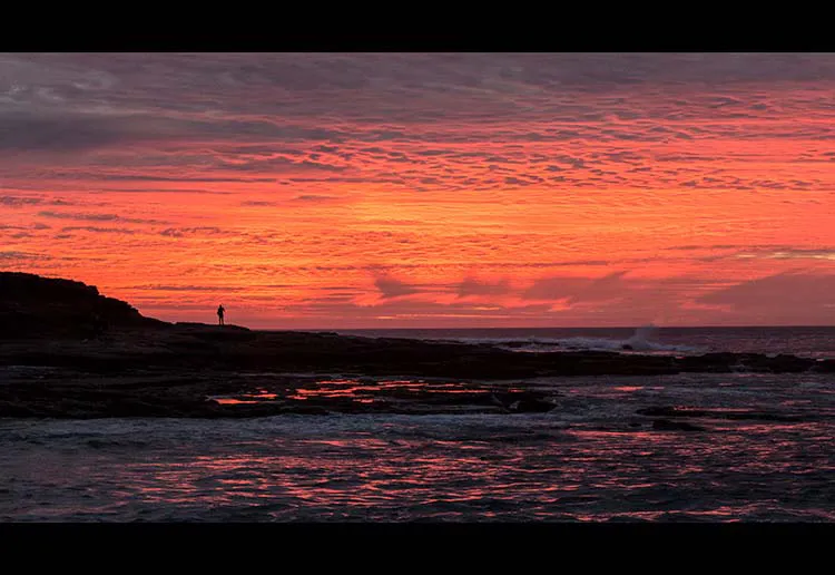 Landscape Photo of a beach view during sunset with a bright red, orange and pink skyline.